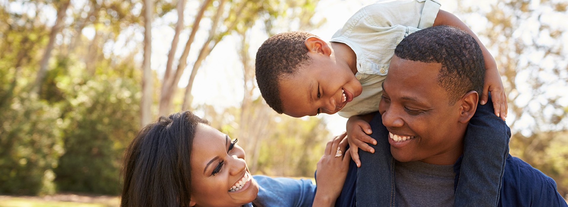 Parents-Carrying-Son-On-Shoulders-As-They-Walk-In-Park